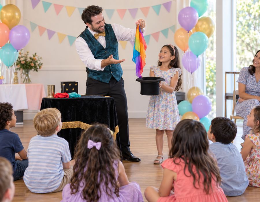 Magician performing to a seated group of children, one child assisting at the front